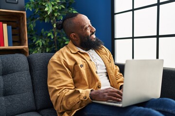 Poster - Young african american man using smartphone sitting on sofa at home