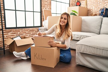 Canvas Print - Young blonde woman smiling confident writing on book at new home