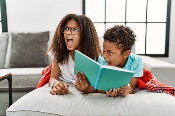 Sticker - Two siblings lying on the sofa reading a book angry and mad screaming frustrated and furious, shouting with anger. rage and aggressive concept.