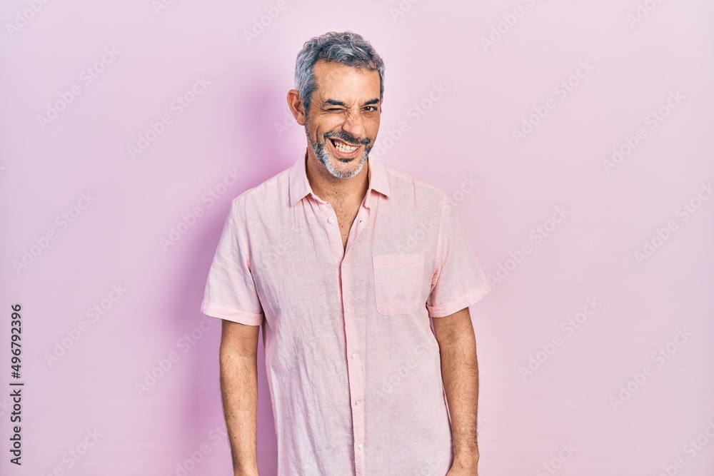 Handsome middle age man with grey hair wearing casual shirt winking looking at the camera with sexy expression, cheerful and happy face.