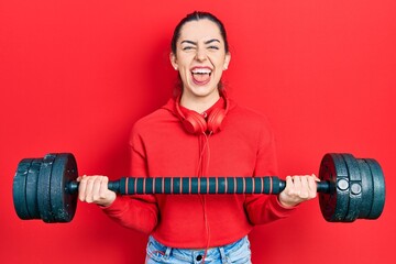 Sticker - Beautiful woman with blue eyes wearing sportswear using dumbbells sticking tongue out happy with funny expression.