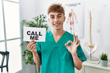 Sticker - Young caucasian physio man holding call me banner at the clinic doing ok sign with fingers, smiling friendly gesturing excellent symbol