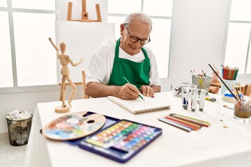 Senior grey-haired artist man smiling happy painting sitting on the table at art studio.