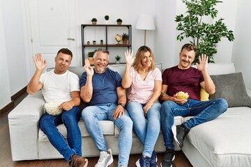 Poster - Group of middle age people sitting on the sofa at home waiving saying hello happy and smiling, friendly welcome gesture