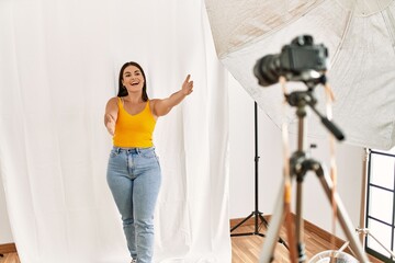 Wall Mural - Young beautiful hispanic woman posing as model at photography studio looking at the camera smiling with open arms for hug. cheerful expression embracing happiness.