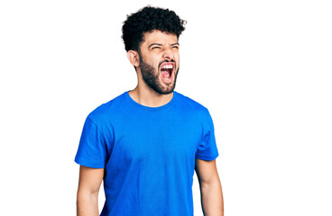 Canvas Print - Young arab man with beard wearing casual blue t shirt angry and mad screaming frustrated and furious, shouting with anger. rage and aggressive concept.