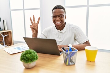 Young african man working at the office using computer laptop showing and pointing up with fingers number three while smiling confident and happy.