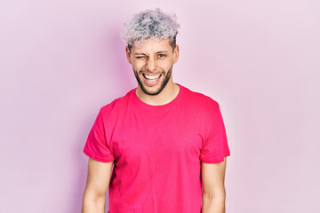 Wall Mural - Young hispanic man with modern dyed hair wearing casual pink t shirt winking looking at the camera with sexy expression, cheerful and happy face.