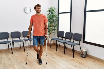 Young hispanic man walking using crutches at clinic waiting room.