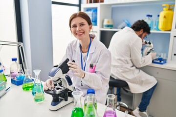 Canvas Print - Young two people working at scientist laboratory looking positive and happy standing and smiling with a confident smile showing teeth