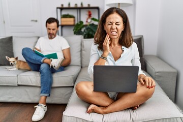 Poster - Hispanic middle age couple at home, woman using laptop touching mouth with hand with painful expression because of toothache or dental illness on teeth. dentist