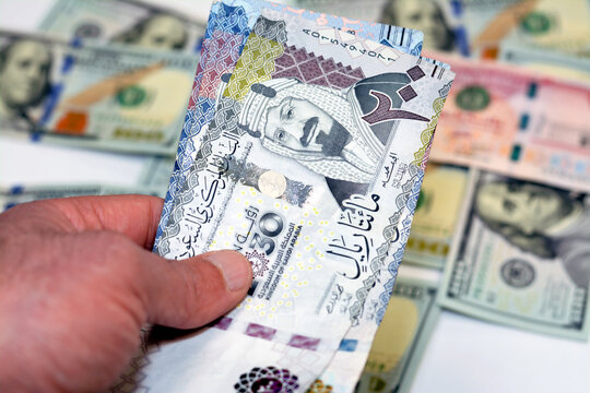 man hand holding a stack of 200 two hundred Saudi riyals banknotes money, spending, giving and using money concept, paying and buying using banknotes on blurred 100 American dollars background