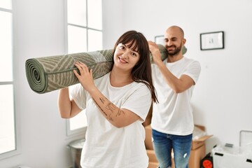 Wall Mural - Young hispanic couple smiling happy holding carpet at new home.