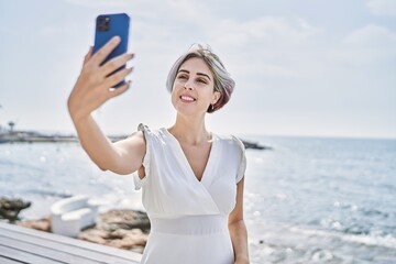 Sticker - Young caucasian girl smiling happy making selfie by the smartphone at the beach.