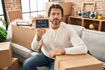 Poster - Handsome middle age man holding blackboard with new home text thinking attitude and sober expression looking self confident