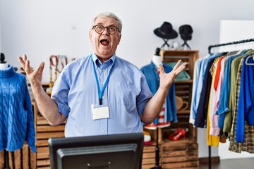 Canvas Print - Senior man with grey hair working as manager at retail boutique crazy and mad shouting and yelling with aggressive expression and arms raised. frustration concept.