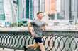 © Anna - Young athlete man runner running at summer morning, background urban city street. Sports training. Fitness cardio workout in fresh air, jogging outside.