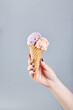Two scoops of ice cream in waffle cone in female hand on gray background