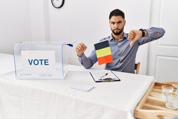 Poster - Young handsome man with beard at political campaign election holding germany flag with angry face, negative sign showing dislike with thumbs down, rejection concept