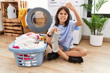 Sticker - Young hispanic girl doing laundry holding socks angry and mad raising fist frustrated and furious while shouting with anger. rage and aggressive concept.