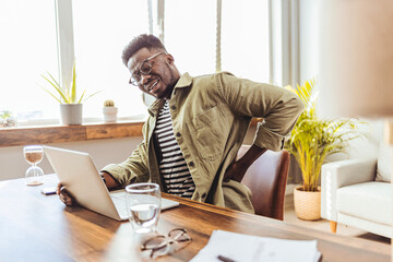 Male businessman who suffers back pain from working from home. Shot of a young businessman suffering from backache while working at his desk during a day at work