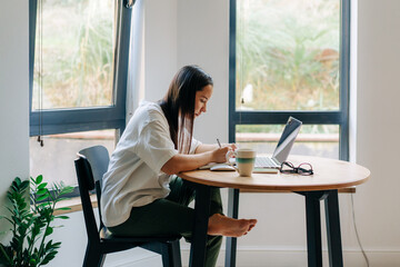 Young woman sitting at desk working remotely from home using laptop