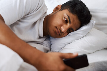 Wall Mural - Still no text back from her. Shot of a young man using his cellphone while lying on his bed.