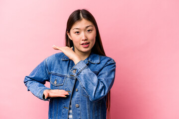 Wall Mural - Young Chinese woman isolated on pink background holding something with both hands, product presentation.