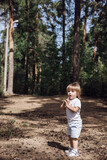 Fototapeta Młodzieżowe - Happy cute toddler boy in t-shirt and shorts walking along path in summer park. Little kid outing on path in pine forest. Hyper-local travel concept. Active lifestyle. Child having fun in green woods.
