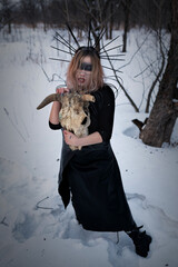 A Scandinavian pagan witch in a crown and a long dress with a cleavage, from which a large breast peeks out, performs a mystical ritual of sacrifice with a bull's skull in a winter snow-covered forest