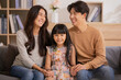 © sopradit - Happy parents and little daughter having fun enjoying spending leisure time together at home sitting on sofa.