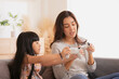 Happy Asian mom teaching daughter to play games with joy stick on sofa in relax day.