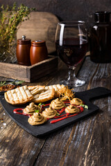 Serving board composition with pate and toast, red sauce and onion chips. On a wooden table is a box with spices and herbs, a glass of red wine. Menu for restaurant, bar, cafe. Сlose up.