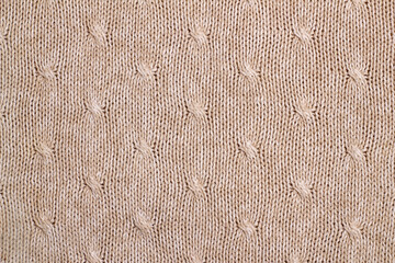 Beige knitted background with pigtails. Texture of a beige wool sweater.