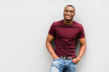 handsome young African American man leaning against gray wall and smiling