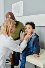 Poster - Experienced mature female endocrinologist in whitecoat checking thyroid of cute little patient visiting clinics with his father