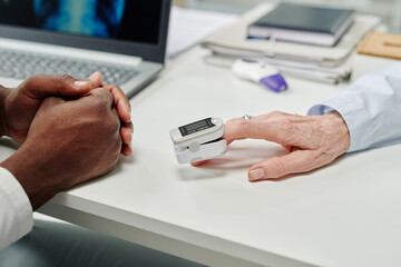Poster - Hand of mature female patient with pulse oximeter on fingertip sitting in front of doctor during check-up of oxygen level in blood