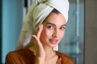 © pressmaster - Young beautiful female with towel on head taking care of her face after bath or morning shower in front of mirror in bathroom