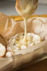 Camembert cheese baked in the oven with garlic sauce and spices. Camembert with croutons in a baking dish. Cheese stretches, drips. Homemade brie in the oven.