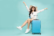Leinwandbild Motiv Asian happy woman sitting on chair with suitcase isolated on green background, Tourist girl having cheerful holiday trip concept