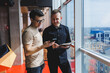 © DSMT - Two male businessman managers stand near the window in a modern office and discuss a new project. Two men with glasses are talking about a new business.