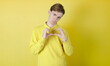 Broken heart guy. Sad guy doing a broken heart with the hands. Isolated on yellow background. Caucasian young guy, 19-20 years old. LOVESICK CONCEPT