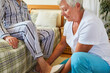 Pflegehilfe hilft Mann mit Demenz beim Hausschuhe anziehen