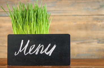 Wall Mural - Menu written with chalk on aged blackboard over spring grass background. Grass over wood. Nature background with grass and wood