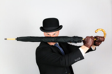 Portrait of British Gentleman in Dark Suit and Bowler Hat Holding Umbrella in Action Pose. Concept of Film Noir Secret Agent Spy Hero.