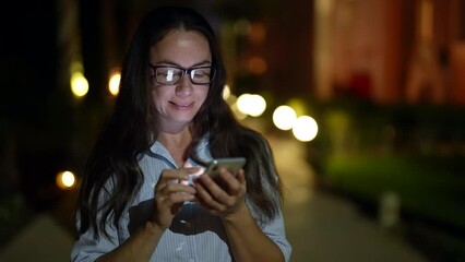 joyful woman is using social media in smartphone during walk in evening, portrait of smiling lady