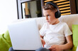 © khmelev - Concentrated schoolboy wearing headphones with laptop play online games at home. Distance learning in quarantine