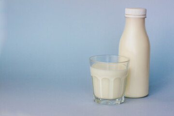 A glass and a bottle of white milk, highlighted on a blue background, close-up.