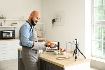 Wall Mural - Handsome man with tasty peach muffins recording video tutorial in kitchen