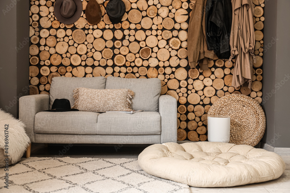 Comfortable sofa, pouf and hangers on wooden wall in room interior